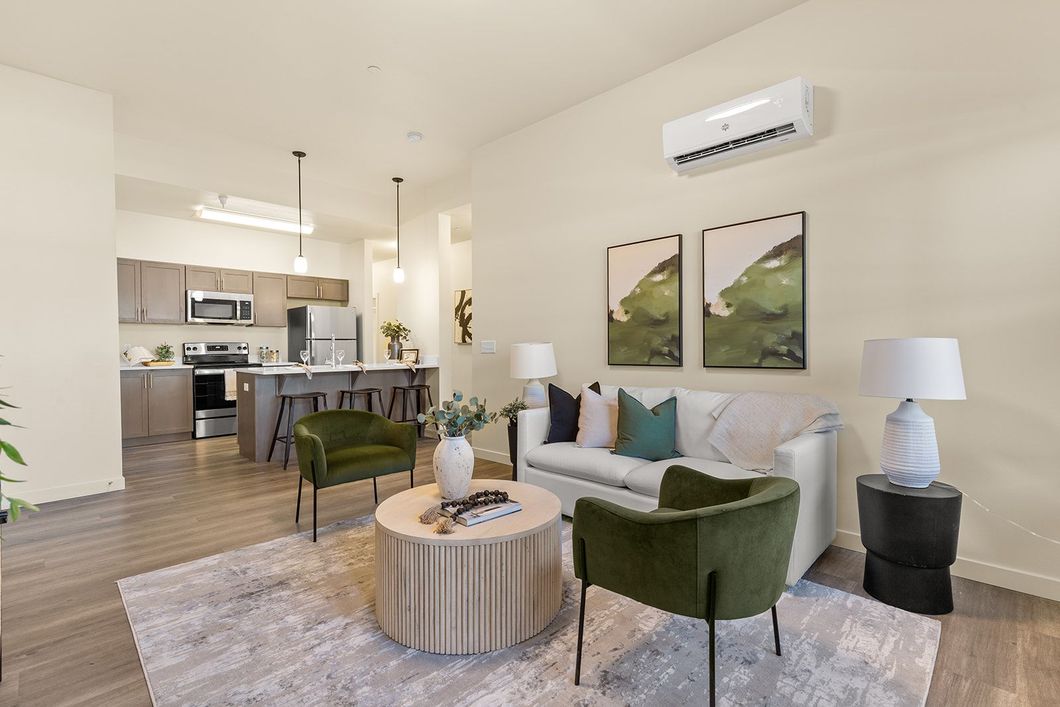 Bright modern living room with green chairs, round coffee table, sofa, and open kitchen behind.