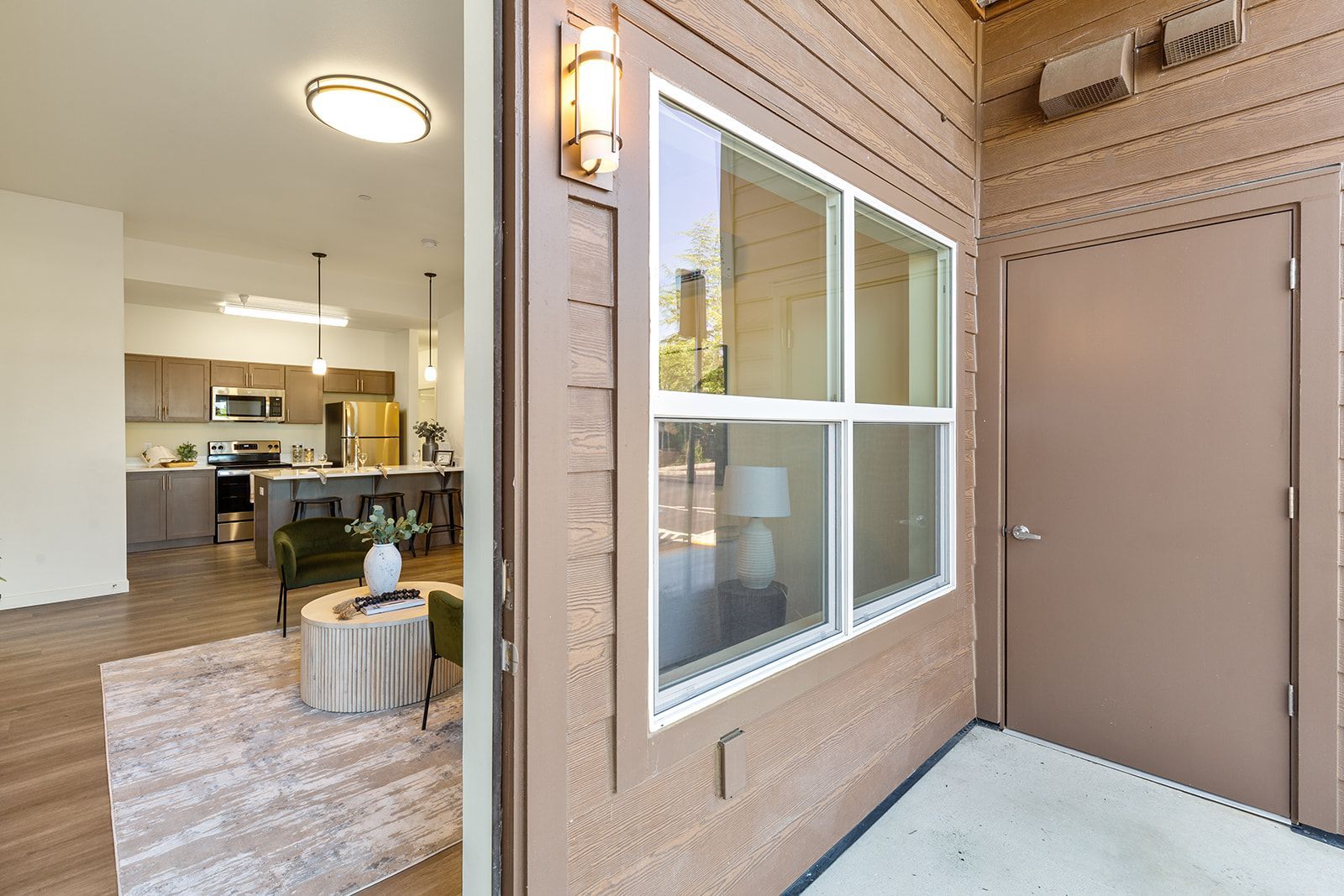 Covered apartment patio with sliding door, window, and view into a bright living room and kitchen.