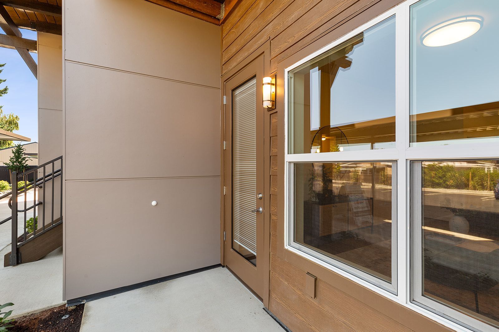 Apartment entryway with beige stucco wall, brick trim, window, and outdoor walkway, seen in warm sunlight