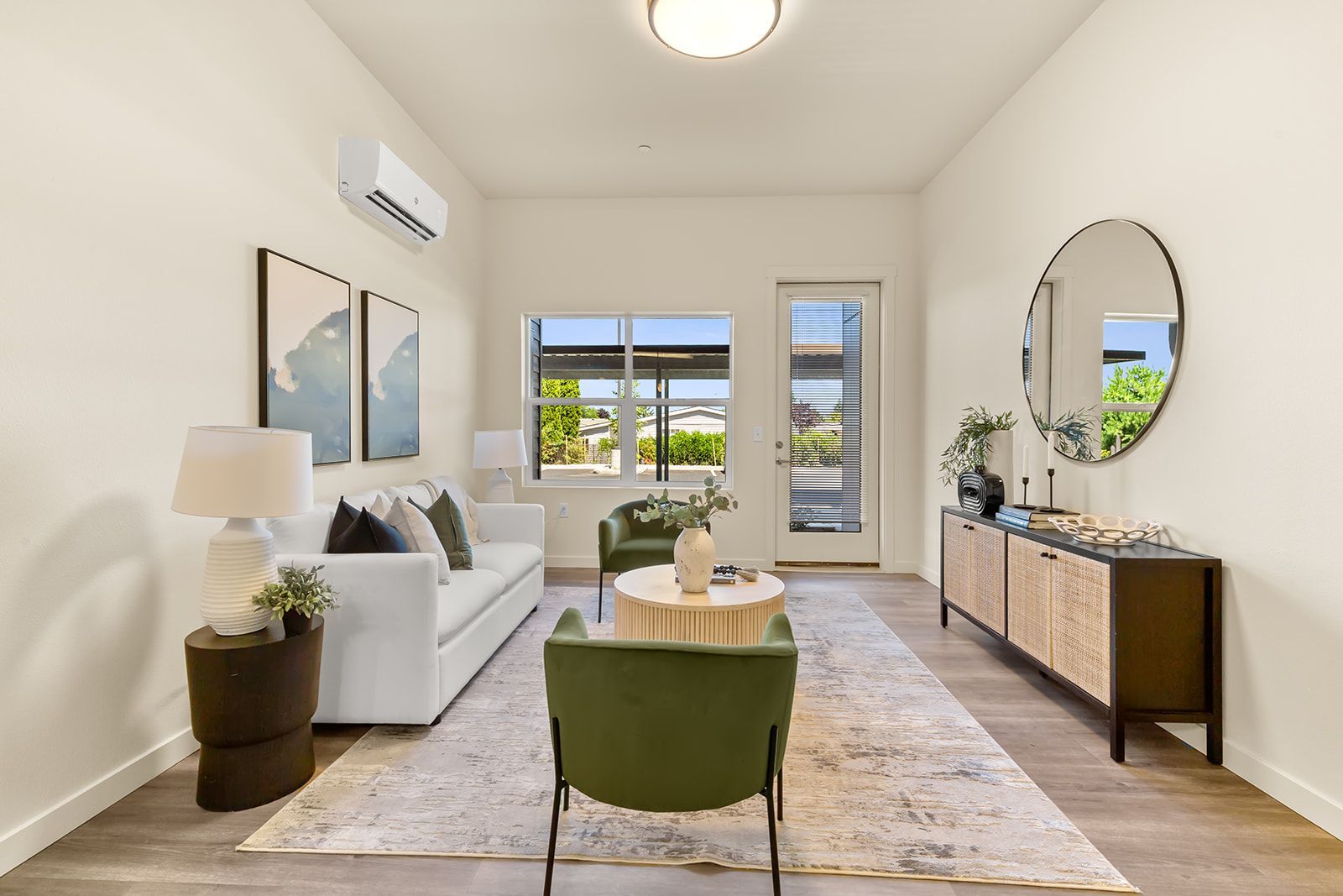 Bright modern living room with white sofa, green chairs, round mirror, and large windows.