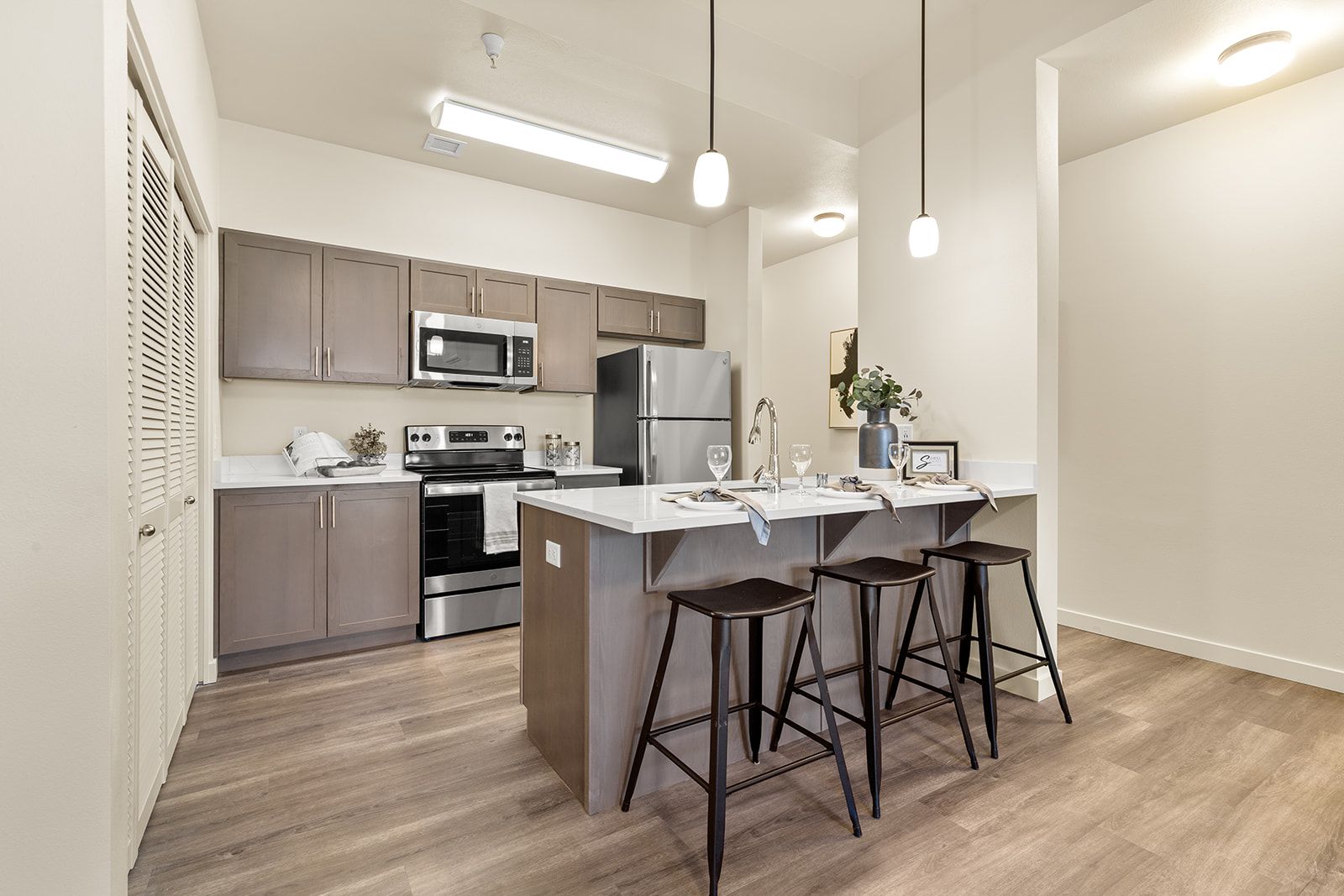 Modern kitchen with island, gray cabinets, stainless appliances, and three bar stools on wood flooring
