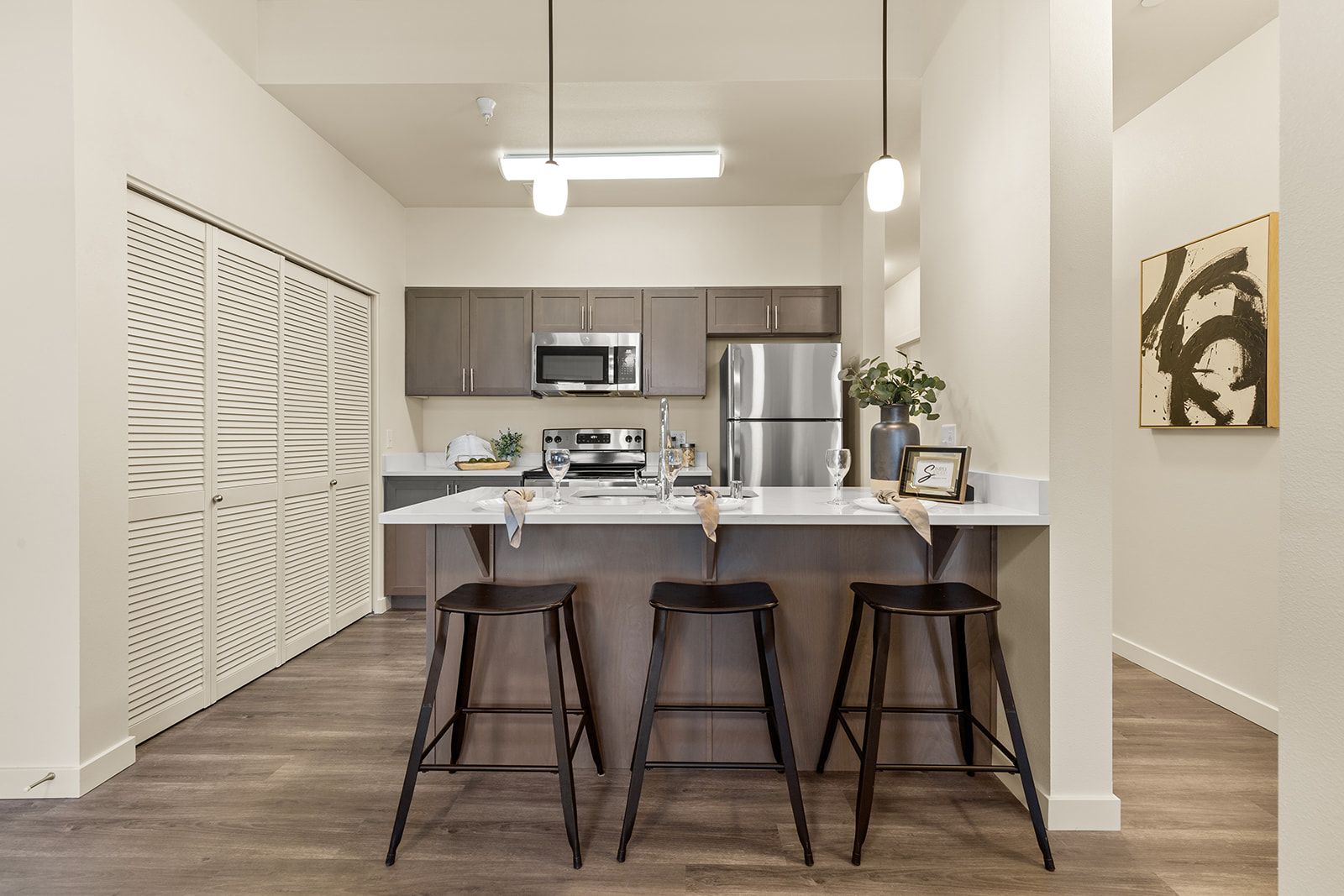 Modern kitchen with island, three stools, stainless steel appliances, and light neutral decor.