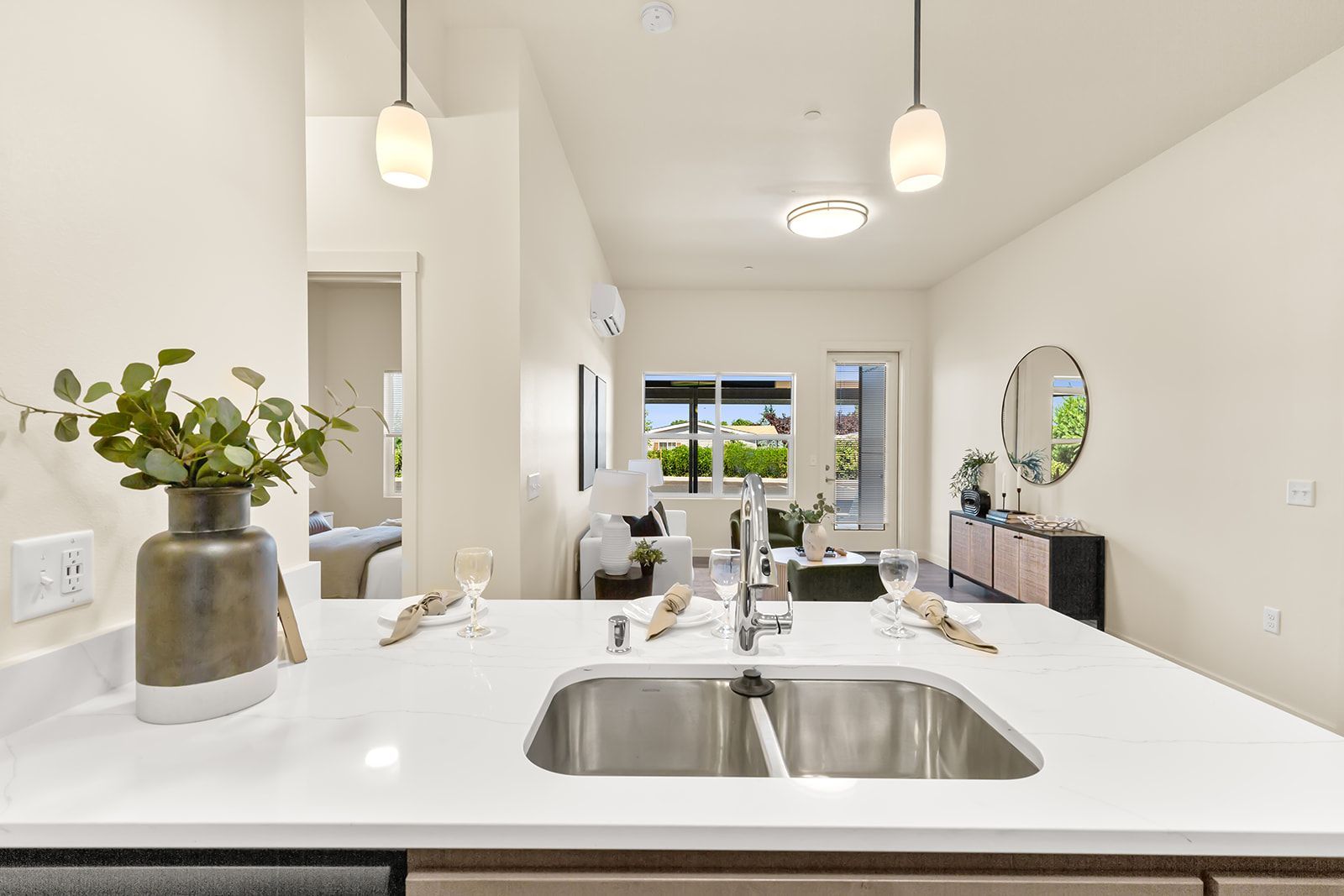 Bright white kitchen island with double sink, pendant lights, and vase of greenery in an open dining area