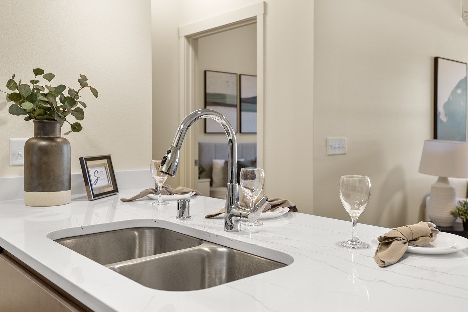Modern kitchen sink with chrome faucet, white countertop, wine glasses, and small decor items