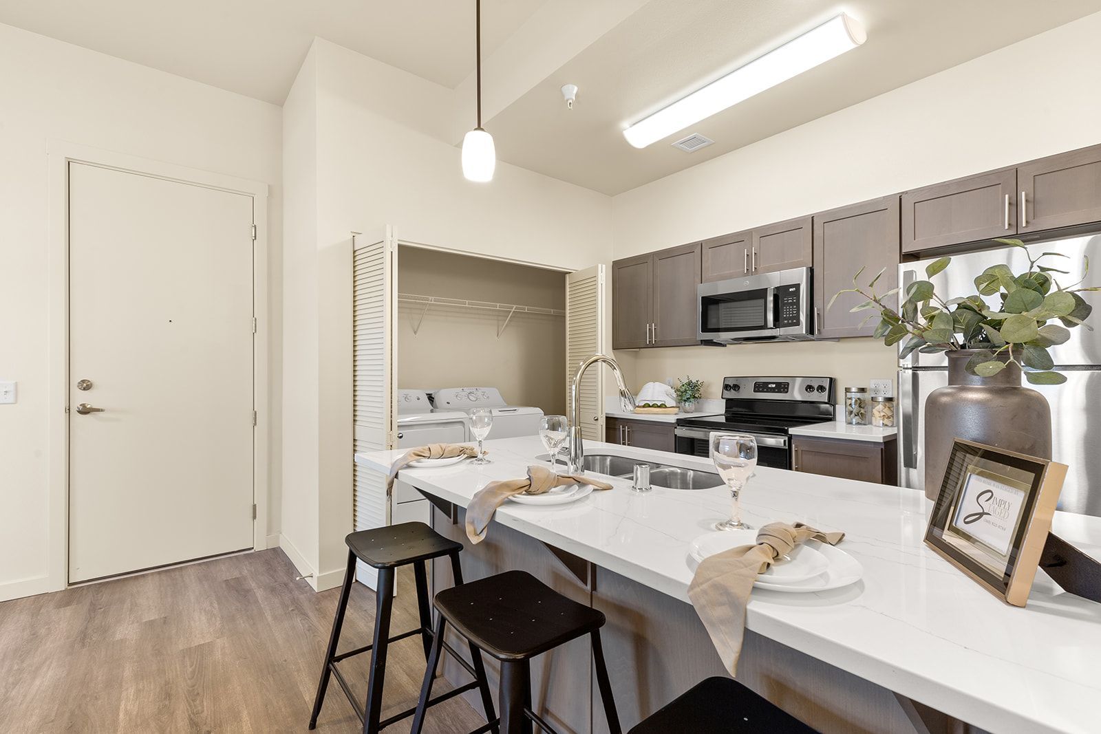 Bright modern kitchen with white island, gray cabinets, dining stools, and a small alcove bed in the background