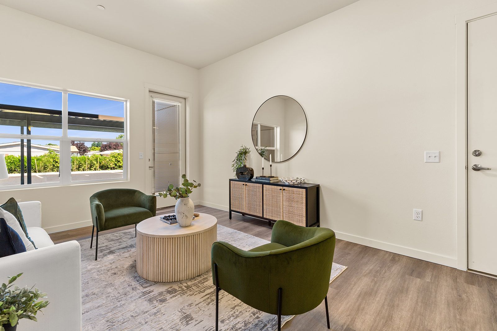 Bright modern living room with green chairs, round coffee table, mirror, and window view of palm trees