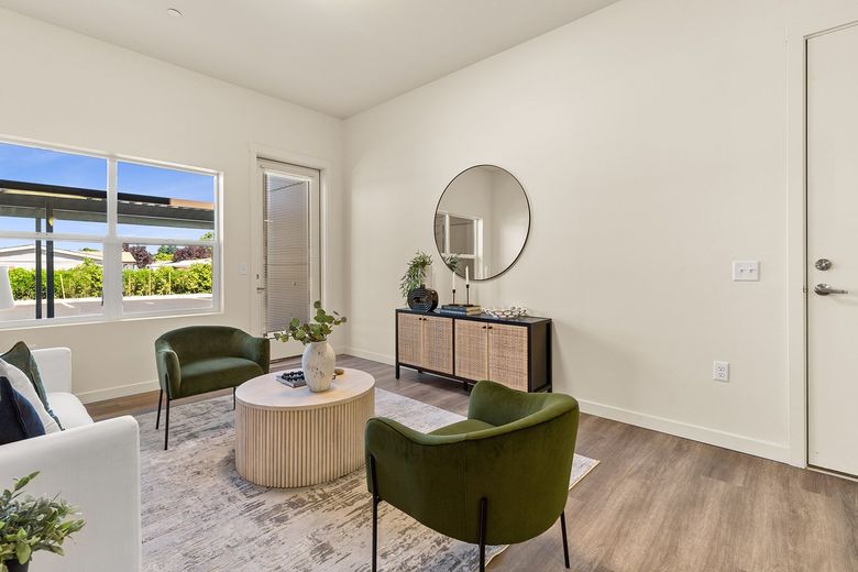 Bright modern living room with green chairs, round coffee table, mirror, and window view of palm trees