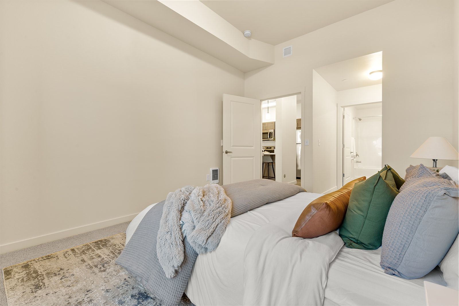 Bright bedroom with white walls, open closet doors, a bed with colorful pillows, and a patterned throw blanket.