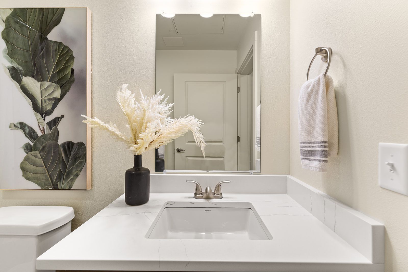 Modern bathroom vanity with white sink, mirror, towel, and floral decor on the counter