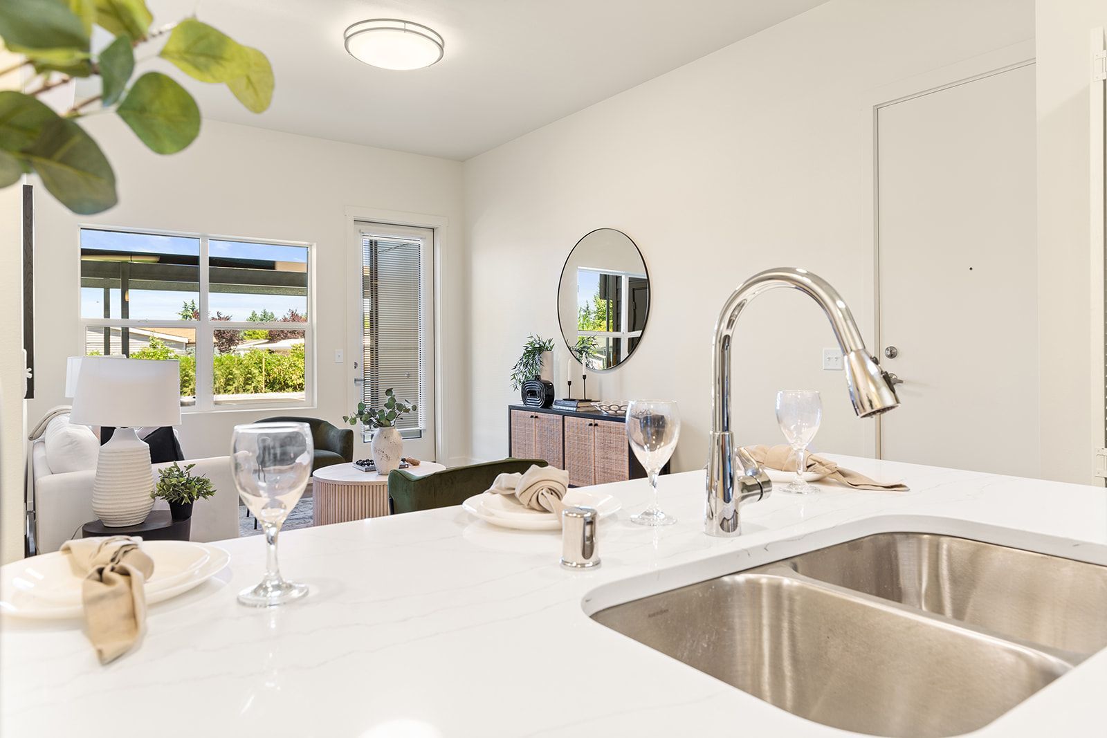 Bright modern kitchen with white countertops, stainless sink, and dining area by open balcony doors