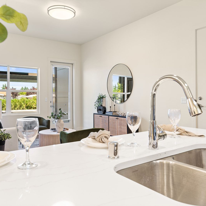 Bright white modern kitchen with island sink, window light, stool, and mirrored decor