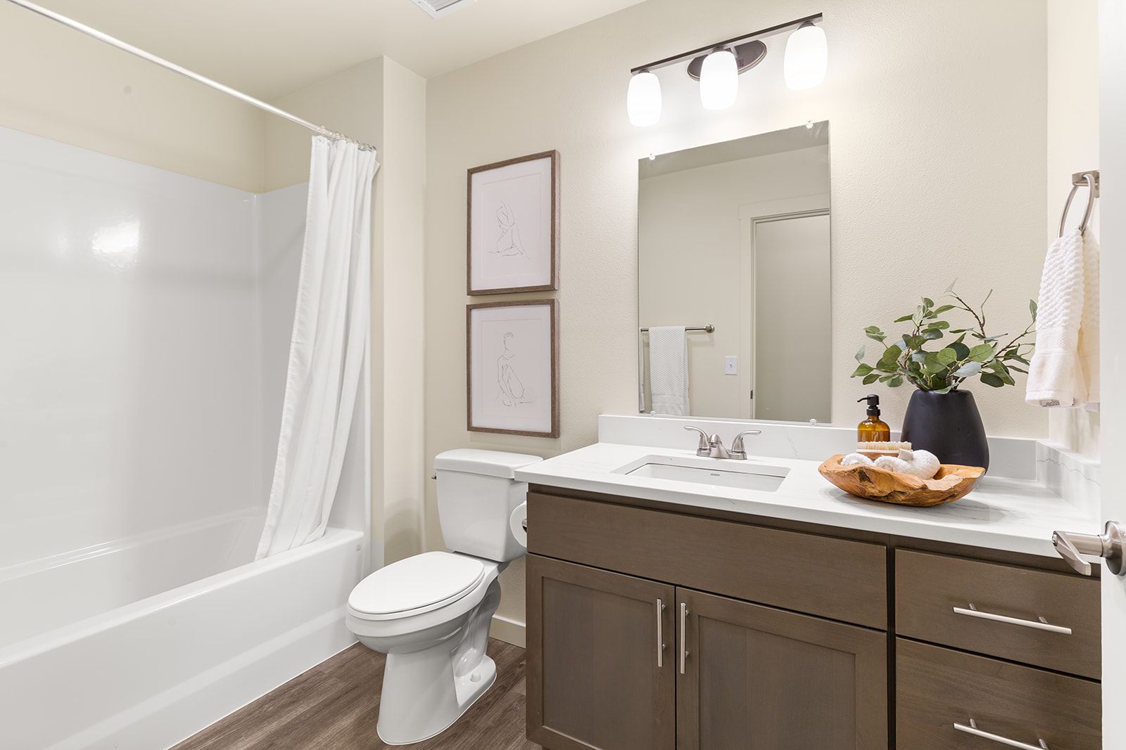 Modern bathroom with bathtub, toilet, dark vanity, mirror, and white shower curtain