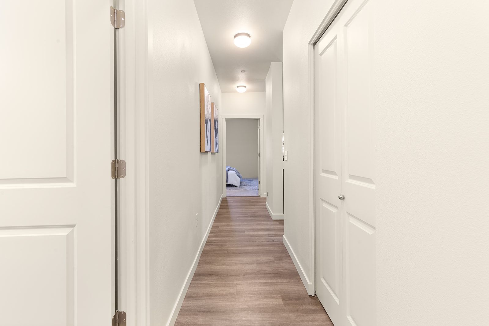Bright white hallway with closed doors, wood floor, and a room at the end.