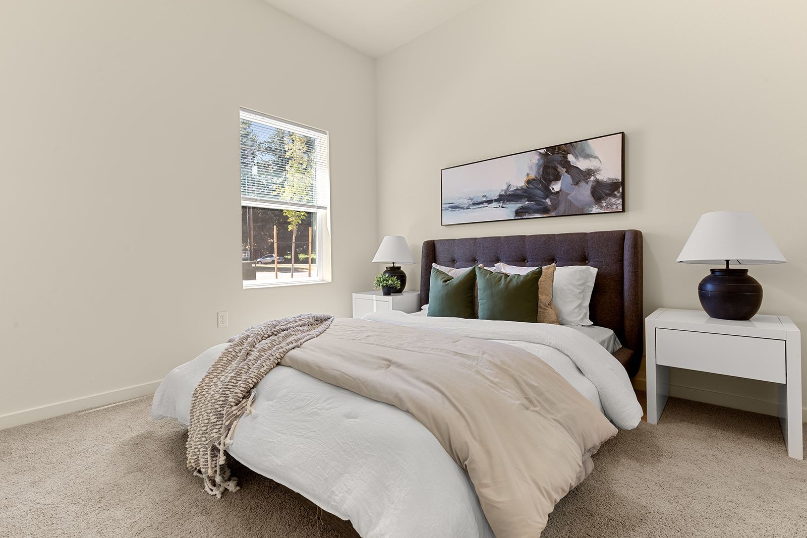 Bright bedroom with a bed, white nightstand, lamps, and a window with blinds