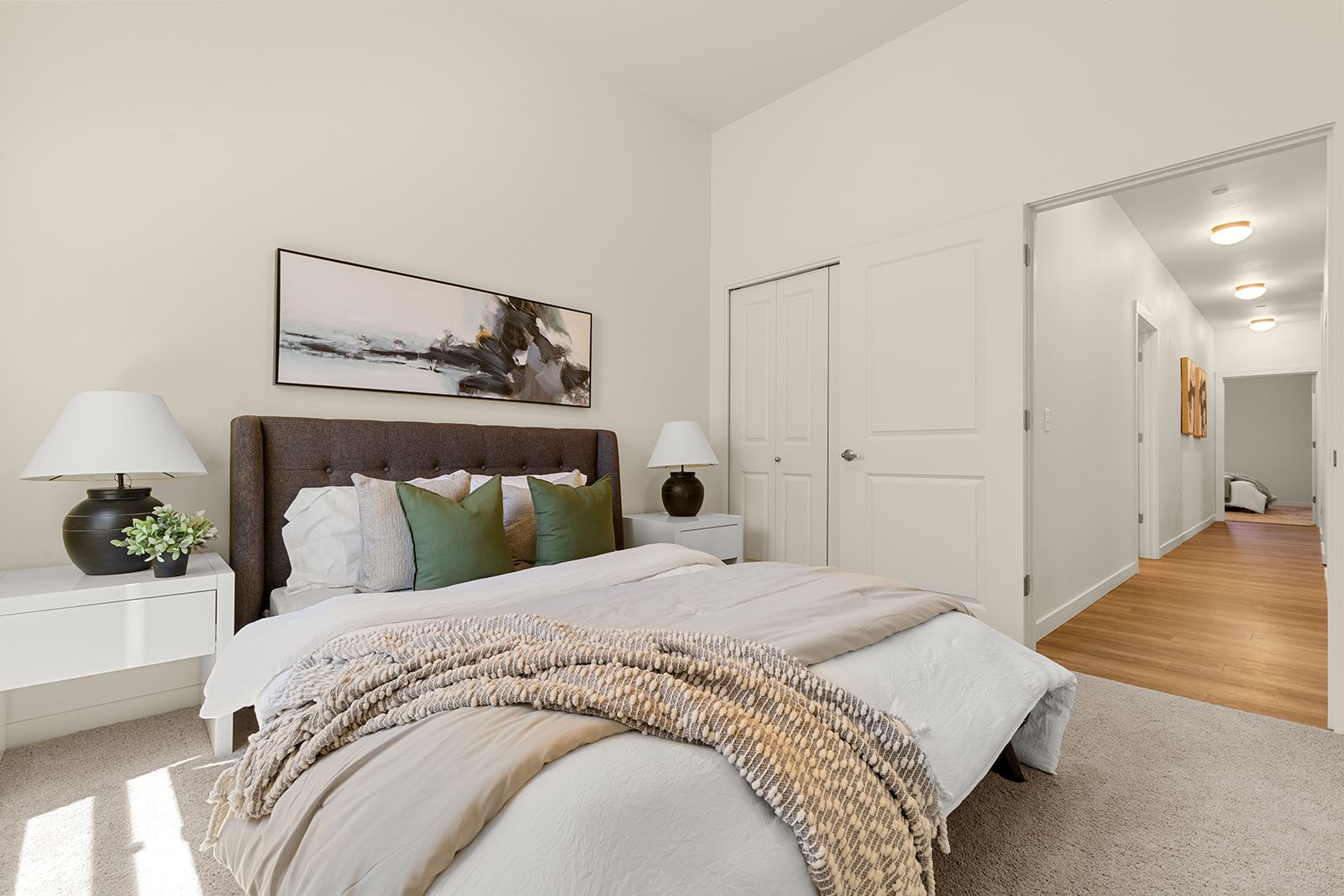 Bright modern bedroom with a king bed, white walls, bedside lamps, and hallway view