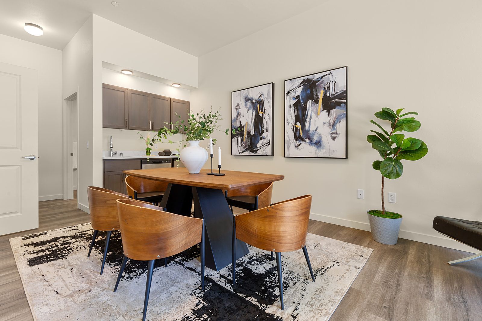Modern dining area with wooden table, tan chairs, abstract wall art, and a potted plant on a rug