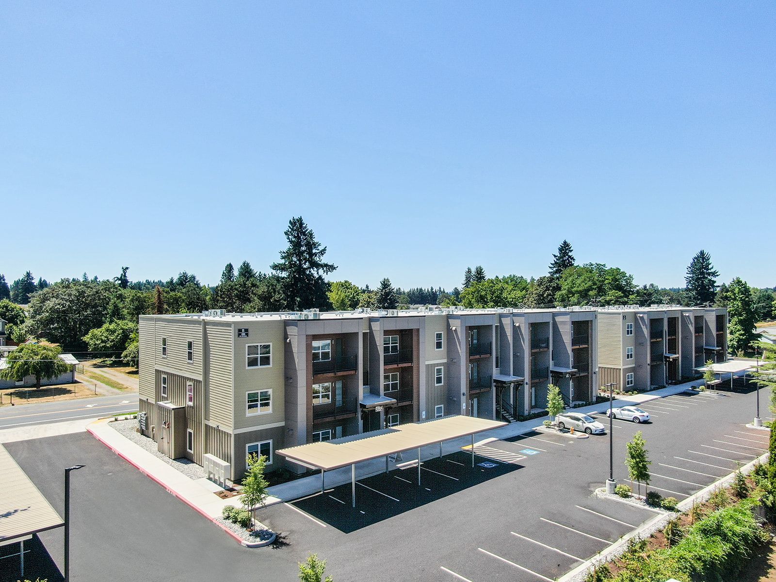 Aerial view of a modern apartment complex with balconies, parking lot, and trees nearby