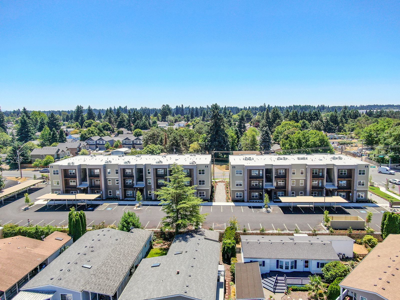 Aerial view of a suburban apartment complex with trees, rooftops, and a clear blue sky