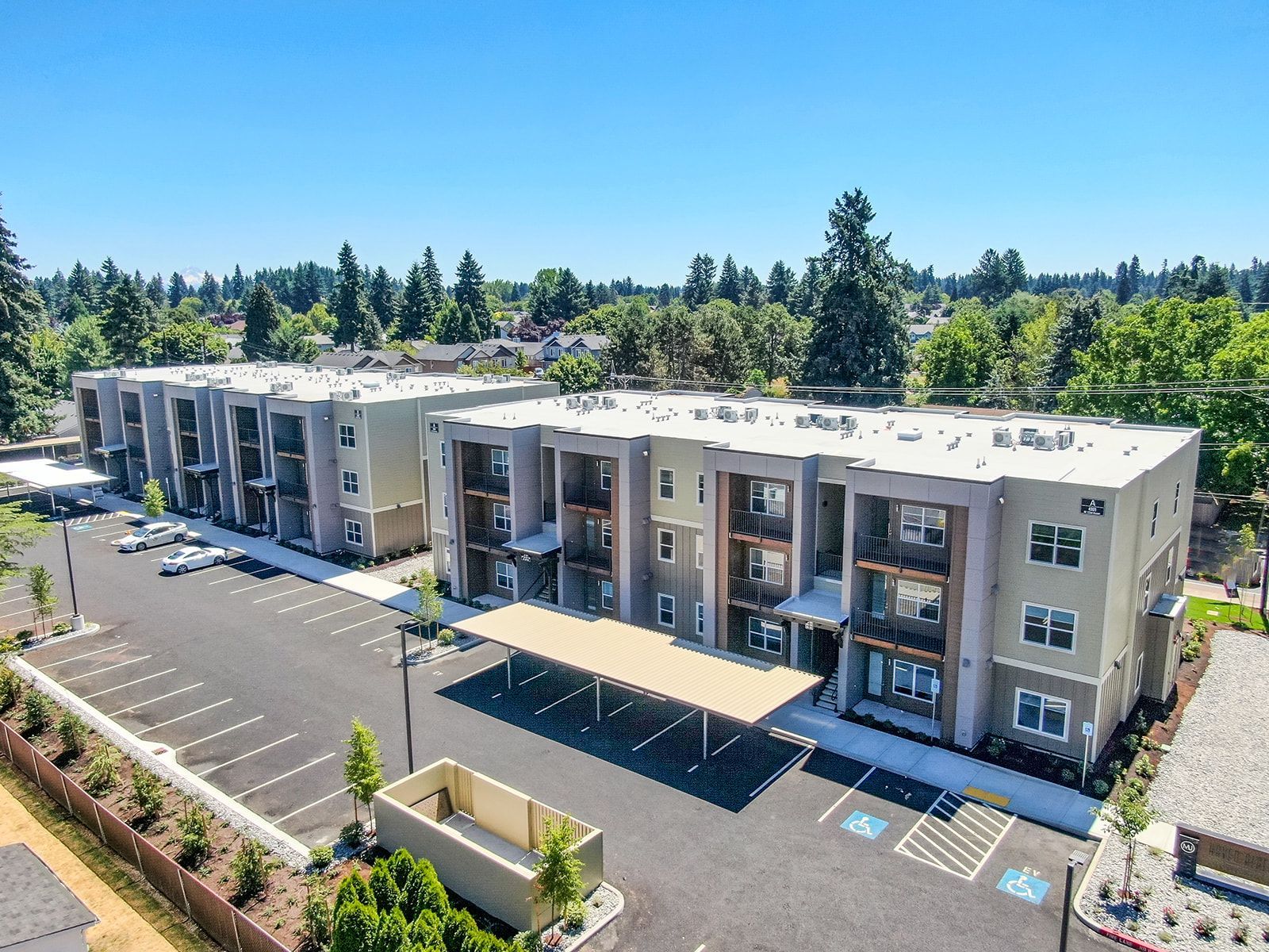 Aerial view of modern apartment buildings with parking lot and blue handicap spaces, surrounded by trees