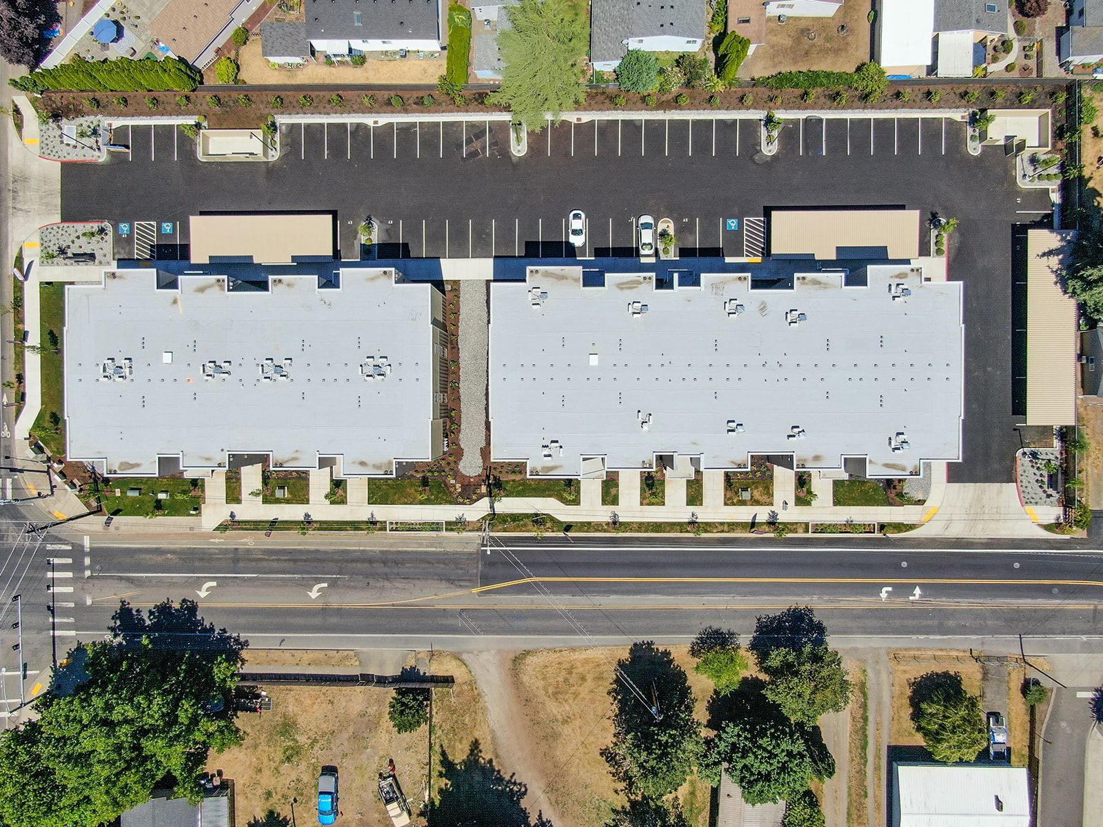 Aerial view of two white apartment buildings with a parking lot and road beside them.
