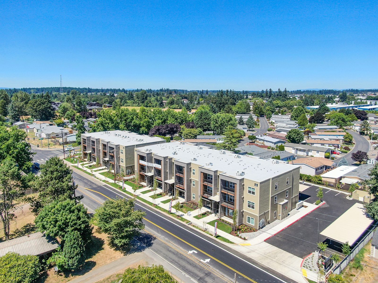 Aerial view of a modern apartment building beside a road, surrounded by trees and neighborhood homes.