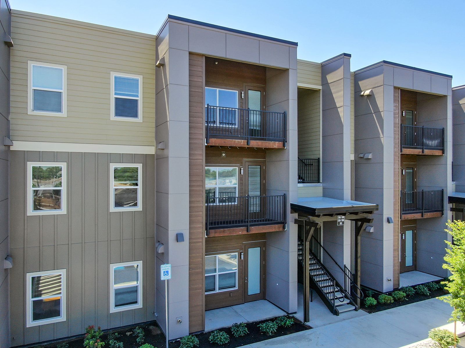 Exterior of a modern apartment building with balconies, beige siding, and exterior stairways