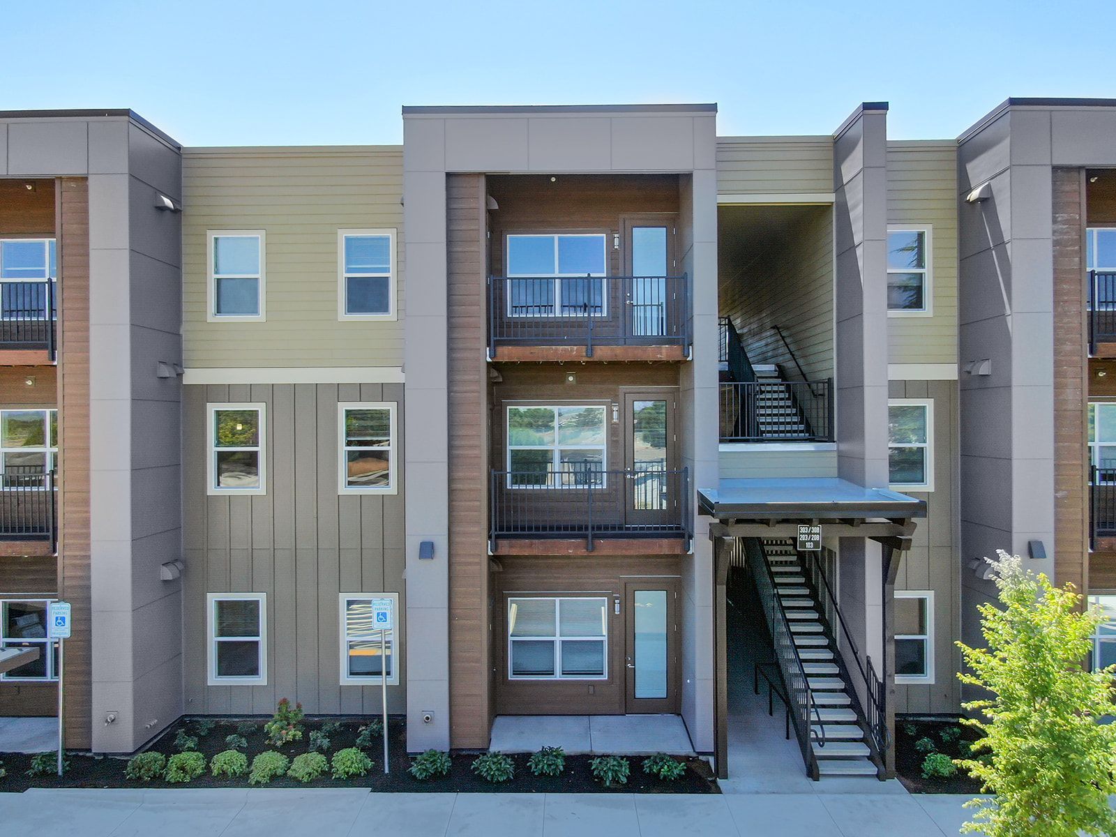 Modern apartment building exterior with balconies, stairways, and beige and gray siding