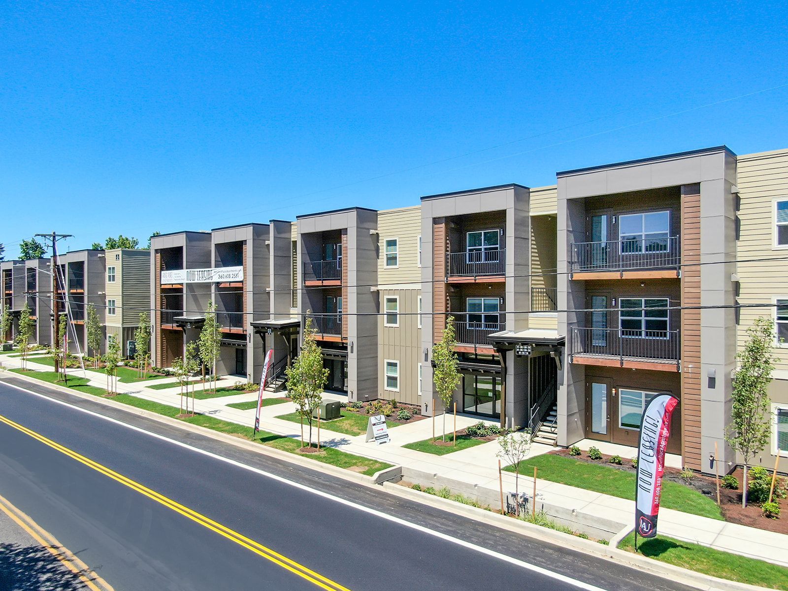 Modern apartment complex beside a wide road under a clear blue sky