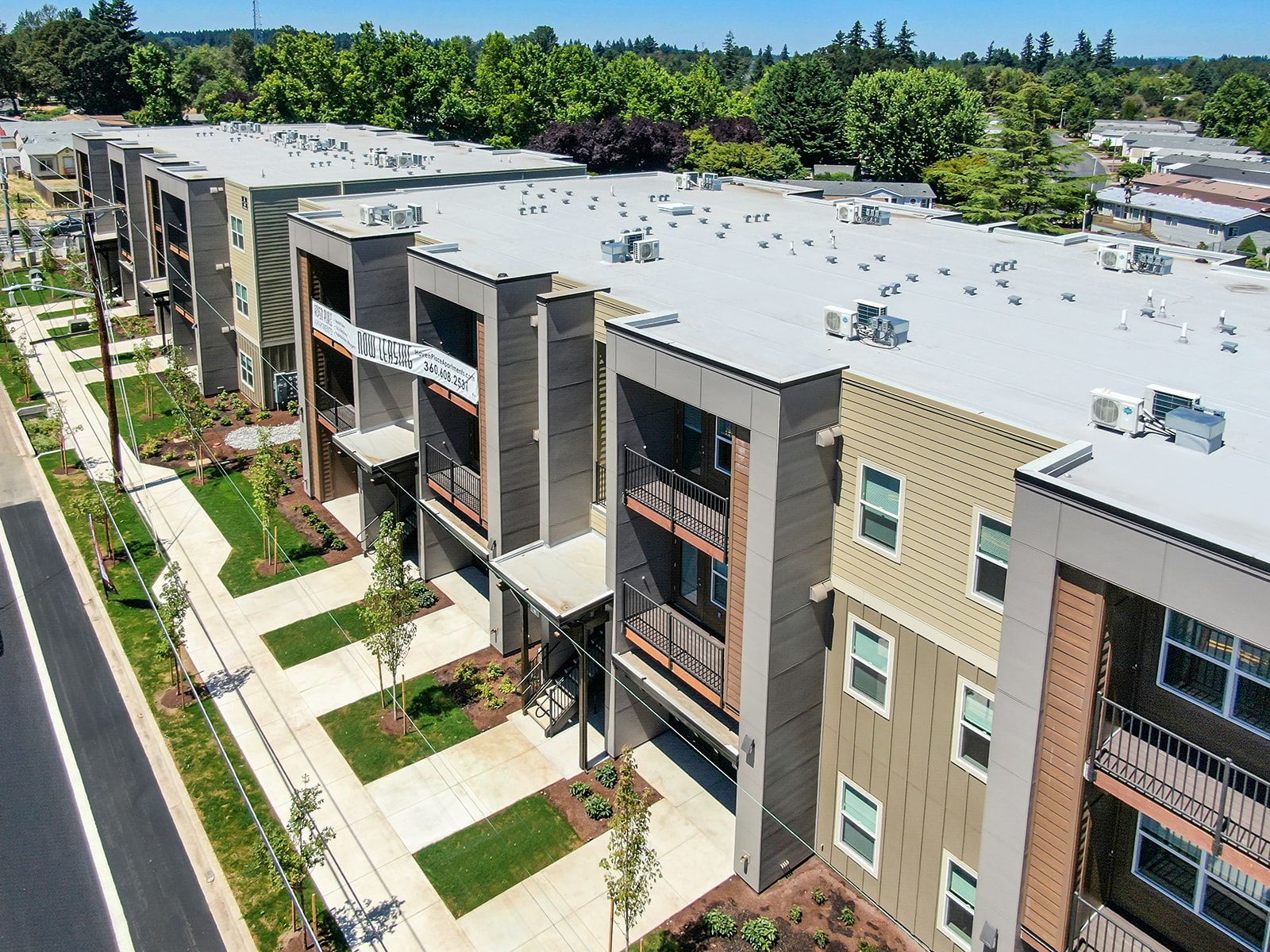Aerial view of modern apartment buildings with balconies, walkways, and trees in a sunny residential complex.