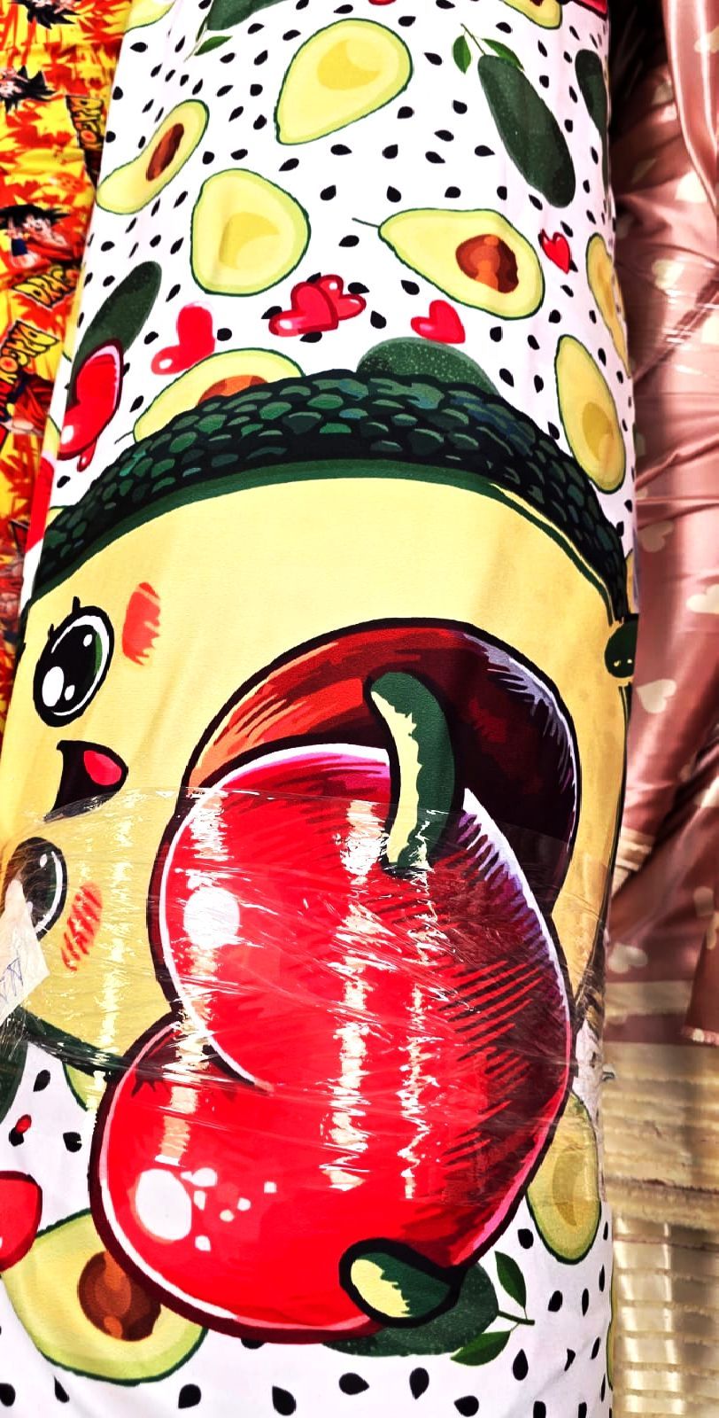 Tela con diseños de aguacate, manzana de dibujos animados con cara y pequeños frutos rojos sobre fondo blanco.