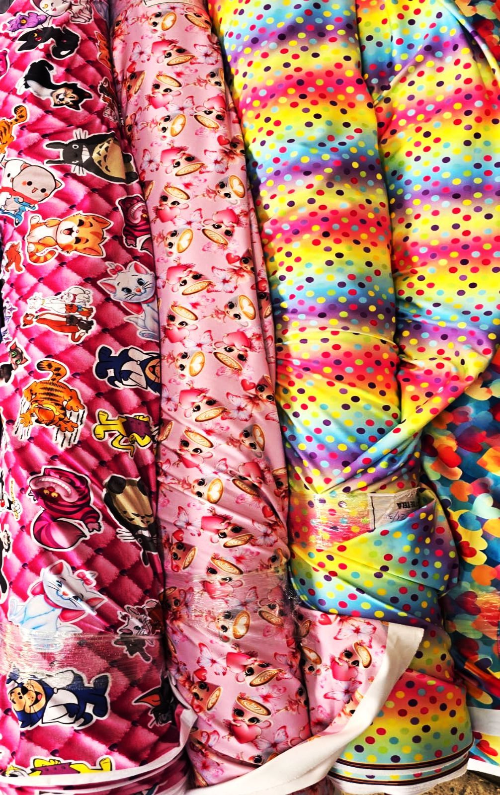 Rollos de tela de colores con distintos patrones: personajes de dibujos animados, lunares y tie-dye de arcoíris.