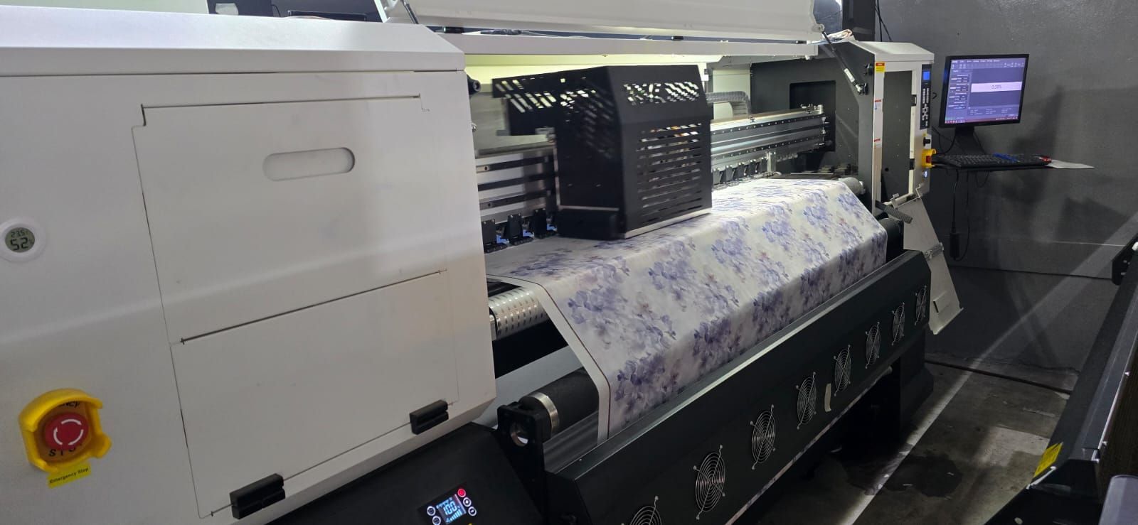 Una gran impresora industrial que imprime un rollo de tela estampada en un entorno de fábrica.