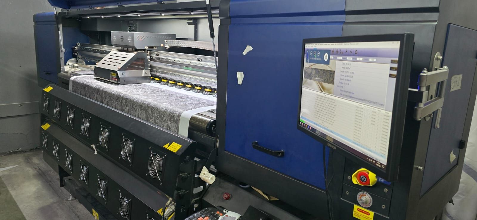 Una gran máquina de impresión industrial con un monitor que muestra datos, ubicada en un almacén.