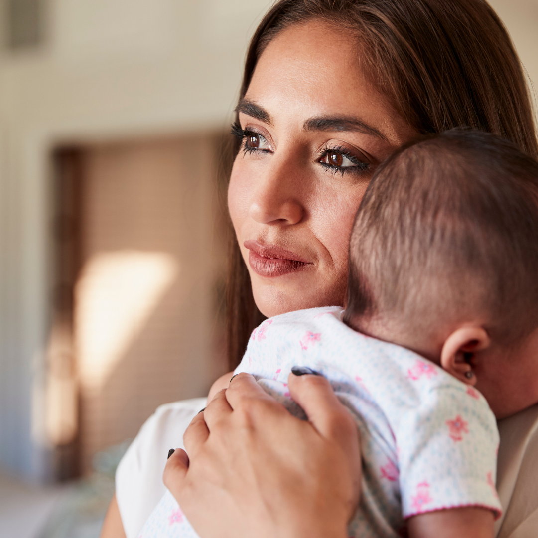 Woman holding a baby, looking off to the side, inside.