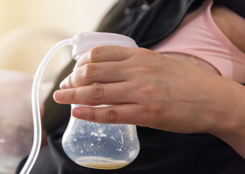 Hand holding a breast milk bottle connected to a white pumping tube