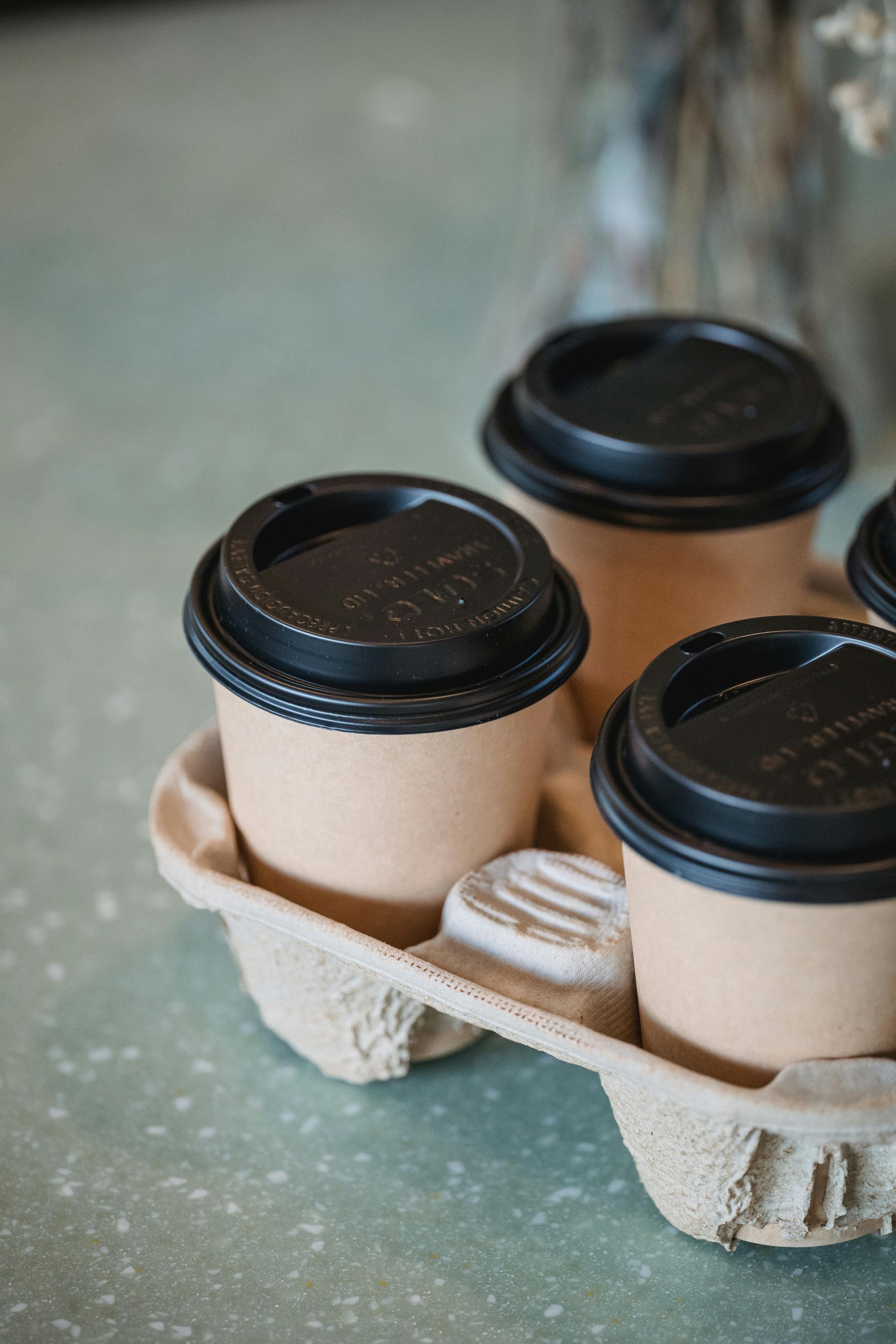 Four takeaway coffee cups in a cardboard carrier on a table.