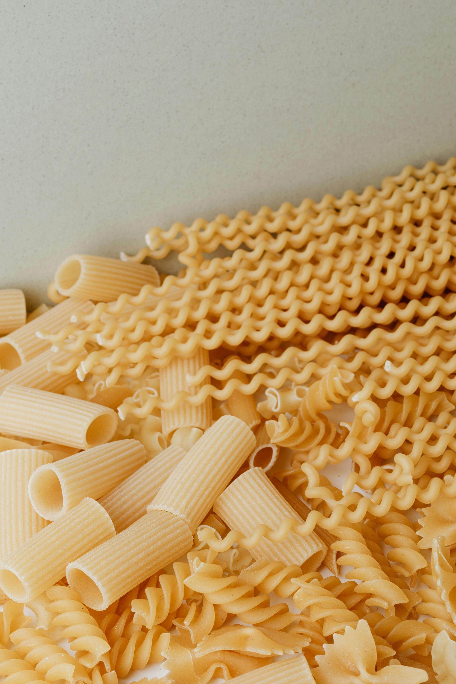 Assorted uncooked pasta shapes, including rigatoni and fusilli, piled on a light surface