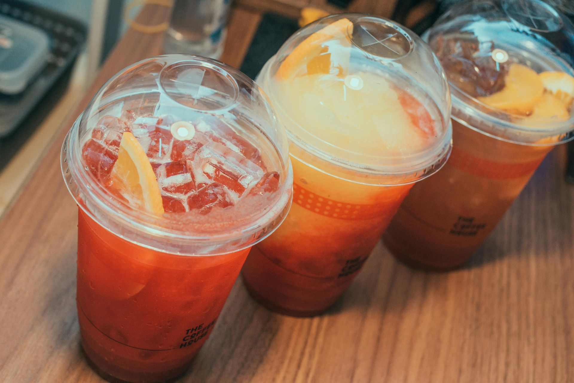 Three iced orange drinks in clear plastic cups on a wooden table