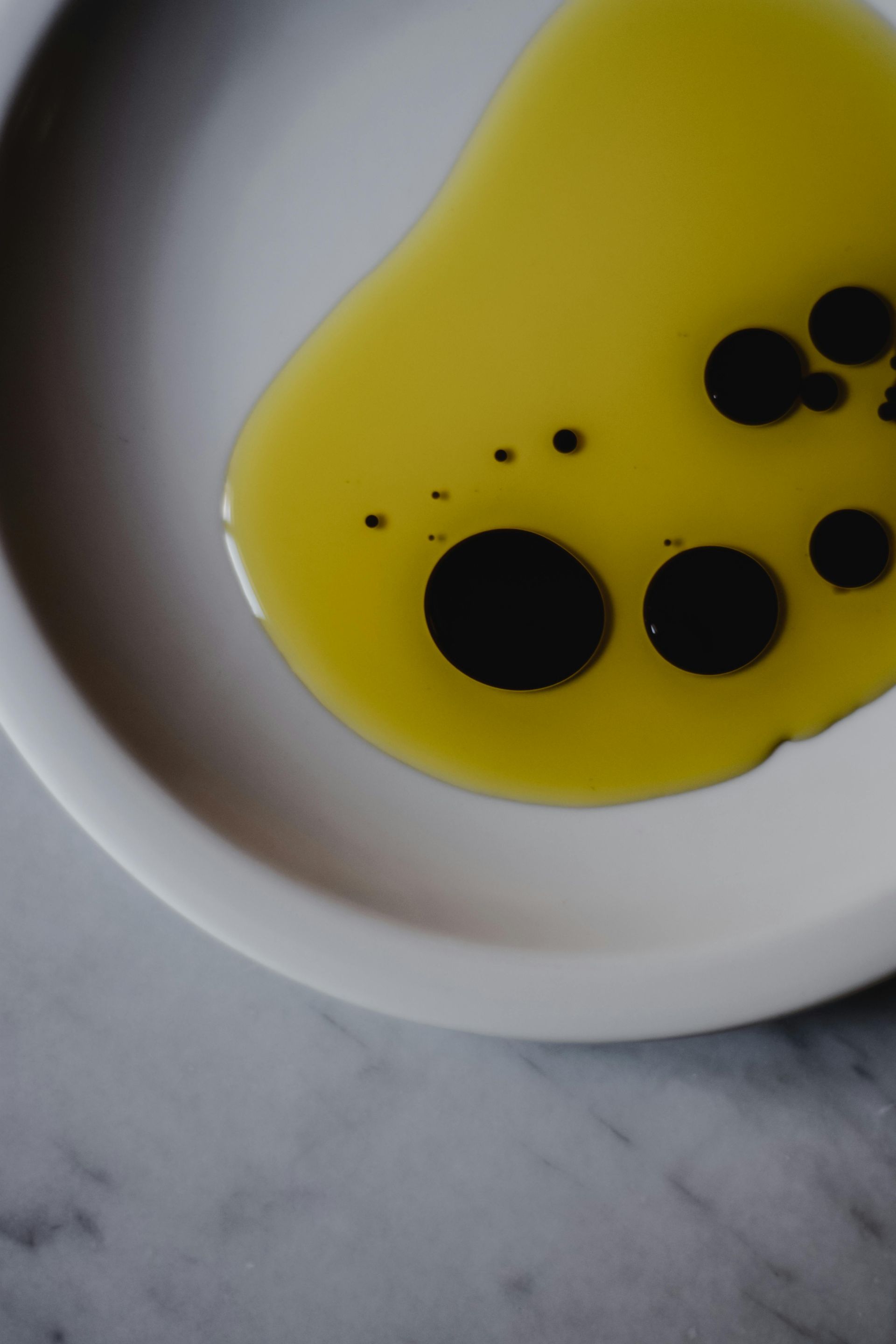 White bowl with yellow oil and scattered black droplets on a marble surface