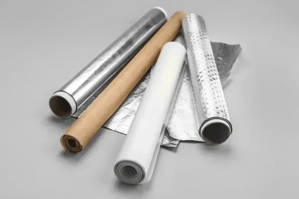 Rolls of aluminum foil, wax paper, and parchment paper on a light gray surface