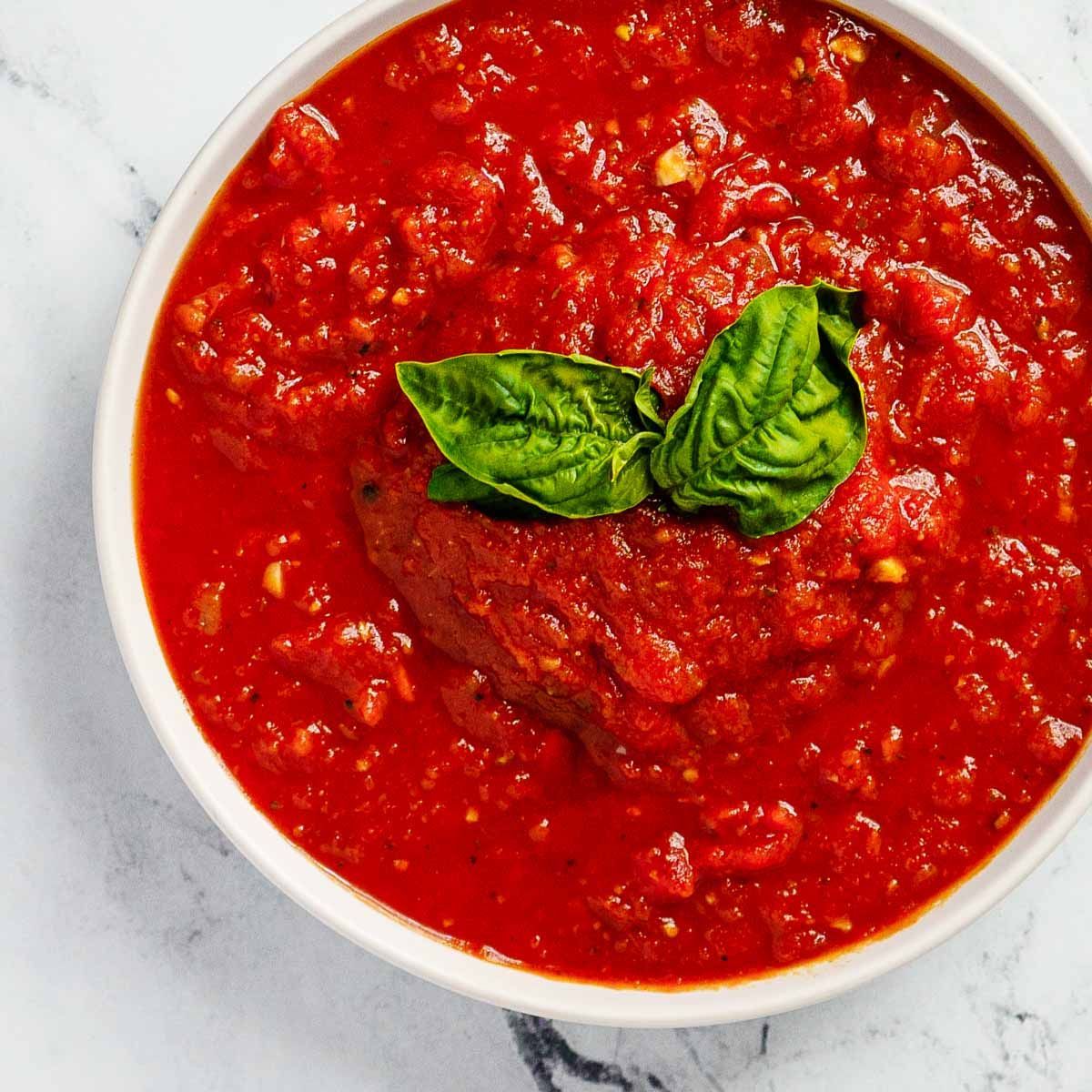 Bowl of chunky red tomato sauce topped with fresh basil leaves