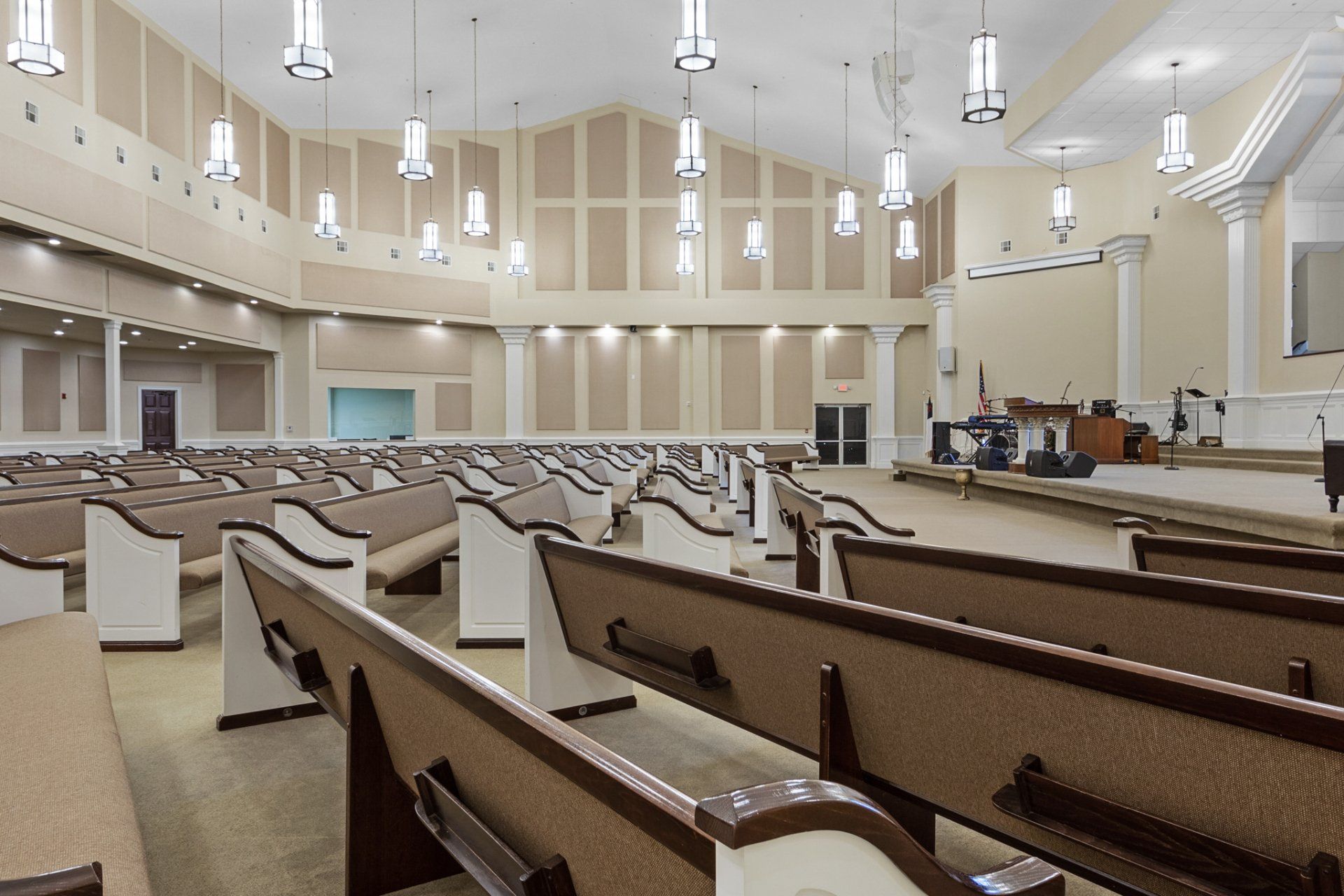 Interior of a beige church sanctuary with rows of pews facing a stage.