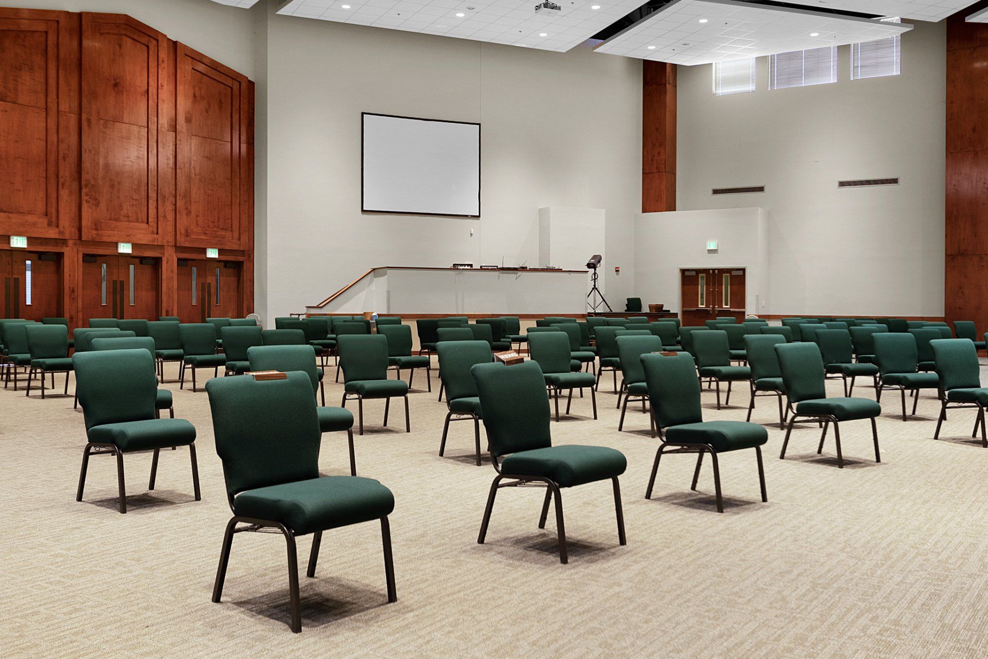 Empty auditorium with rows of green chairs facing a stage with a screen.