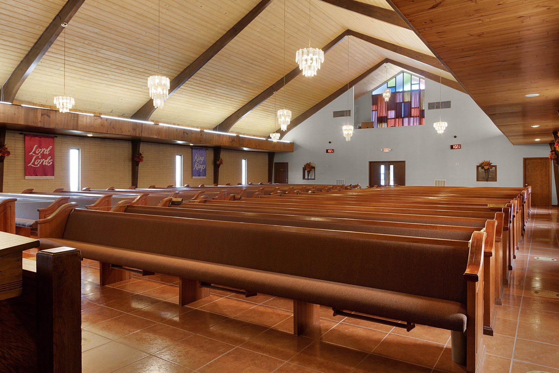 Interior of a church with wooden pews, vaulted ceiling, and stained glass window.