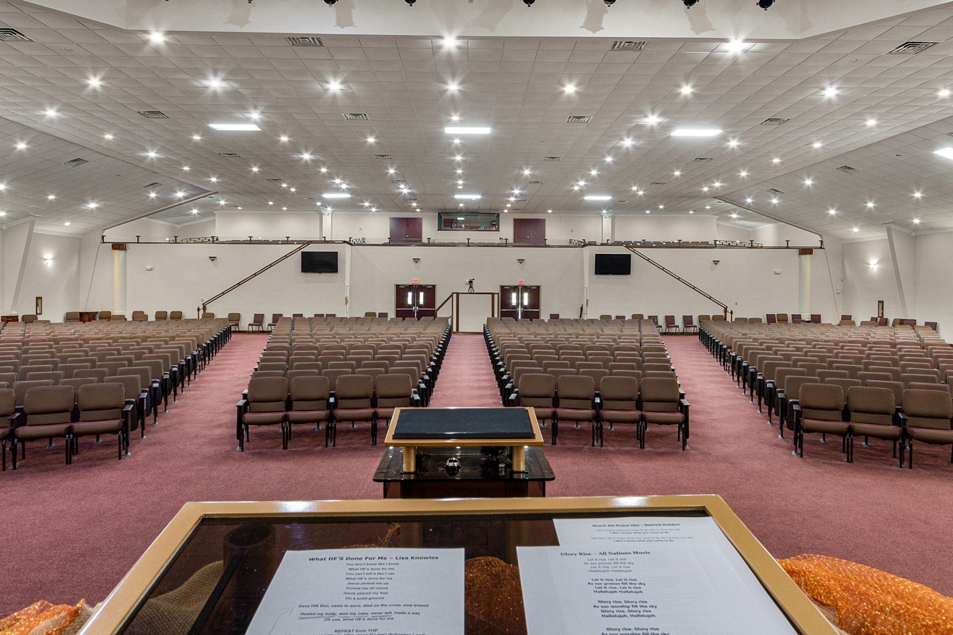 Empty auditorium with rows of seating, stage, and podium, illuminated by bright lights.