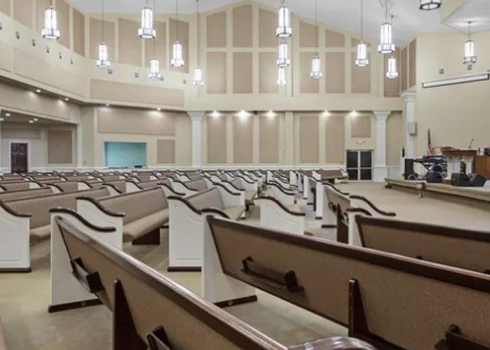Empty church sanctuary with rows of pews, beige walls, and hanging lights.