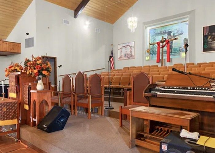 Inside of a church with rows of wooden pews, a stage, and religious decorations.