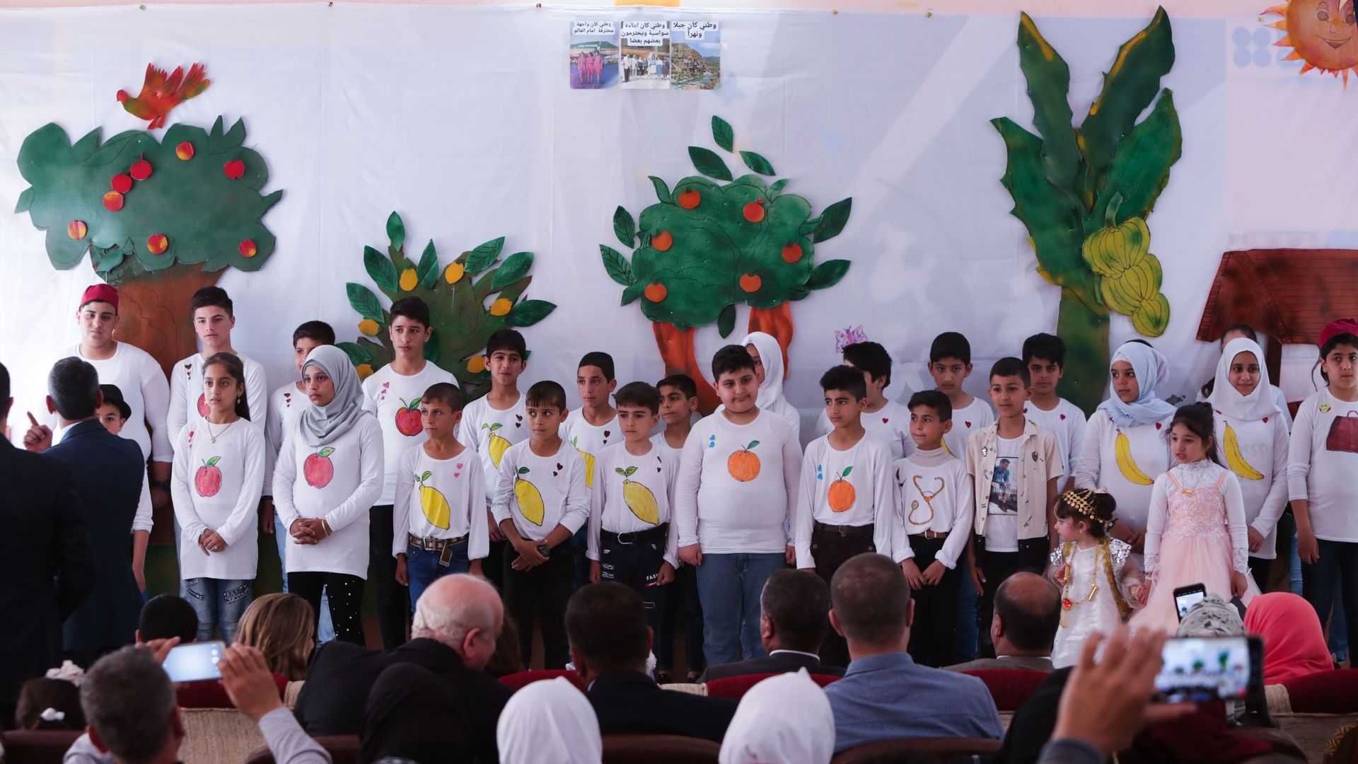 Humanitarian Programs in Iraq: A group of children are standing in front of a wall with trees painted on it