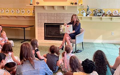 Non Profit: A woman is sitting on the floor reading a book to a group of children.