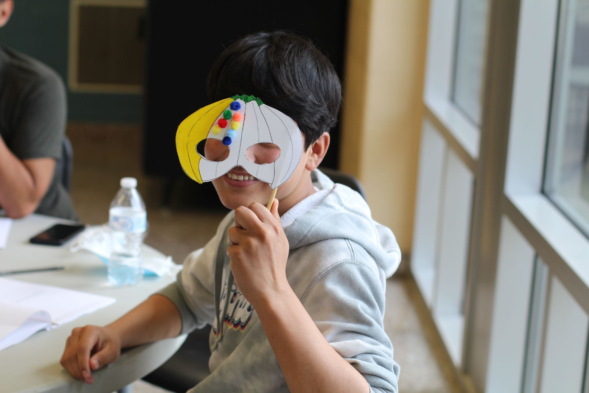 Programs for Refugees: A young boy wearing a paper mask is sitting at a table.